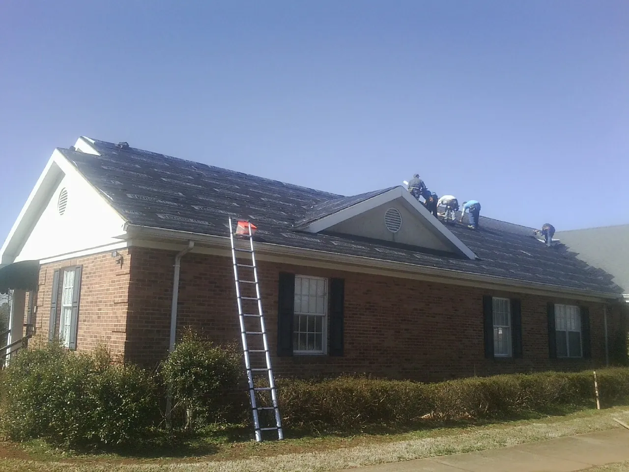 Crew tearing shingles off a brick ranch roof with a ladder set — Emergency Roof Repair work by our crew in Van Buren