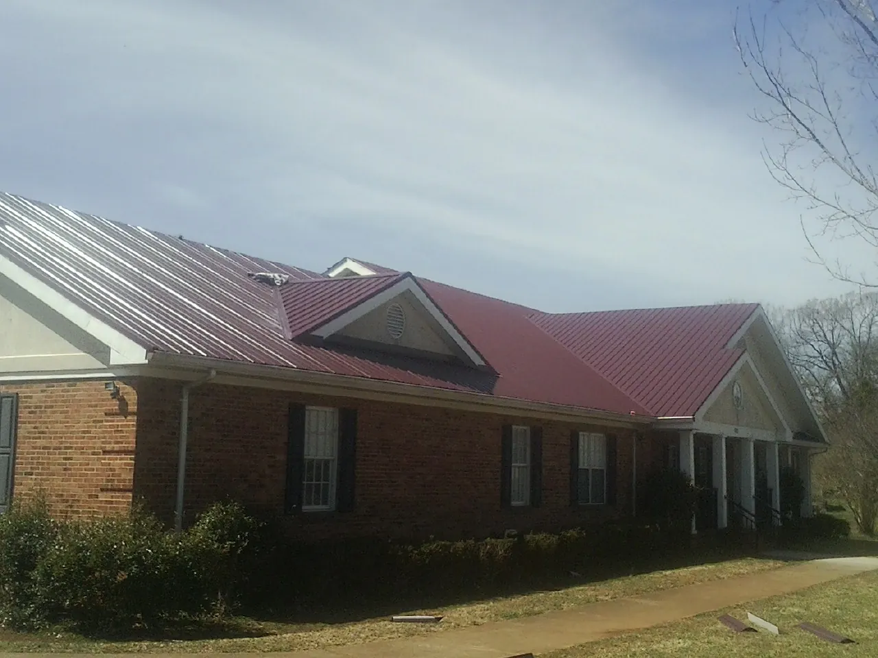 Red metal roof with gabled entries on a long brick building, from a Hail Damage Roof Repair job in Van Buren