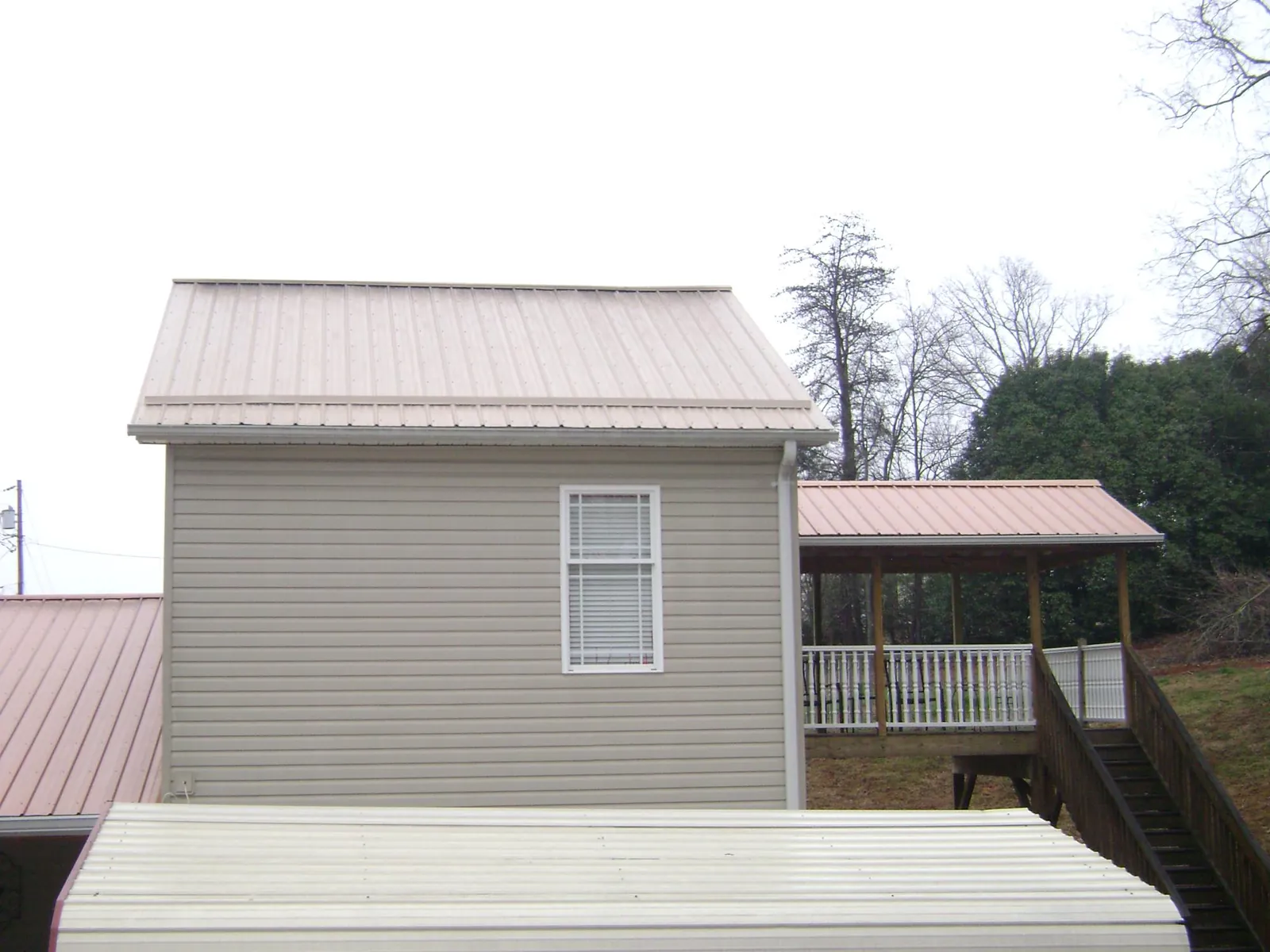 Tan metal roofs on a two story addition and attached porch, from a Roof Replacement job in Van Buren
